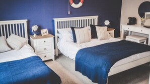 A bedroom with two beds, a nightstand with a lamp, a dresser, and a wall-mounted life preserver.