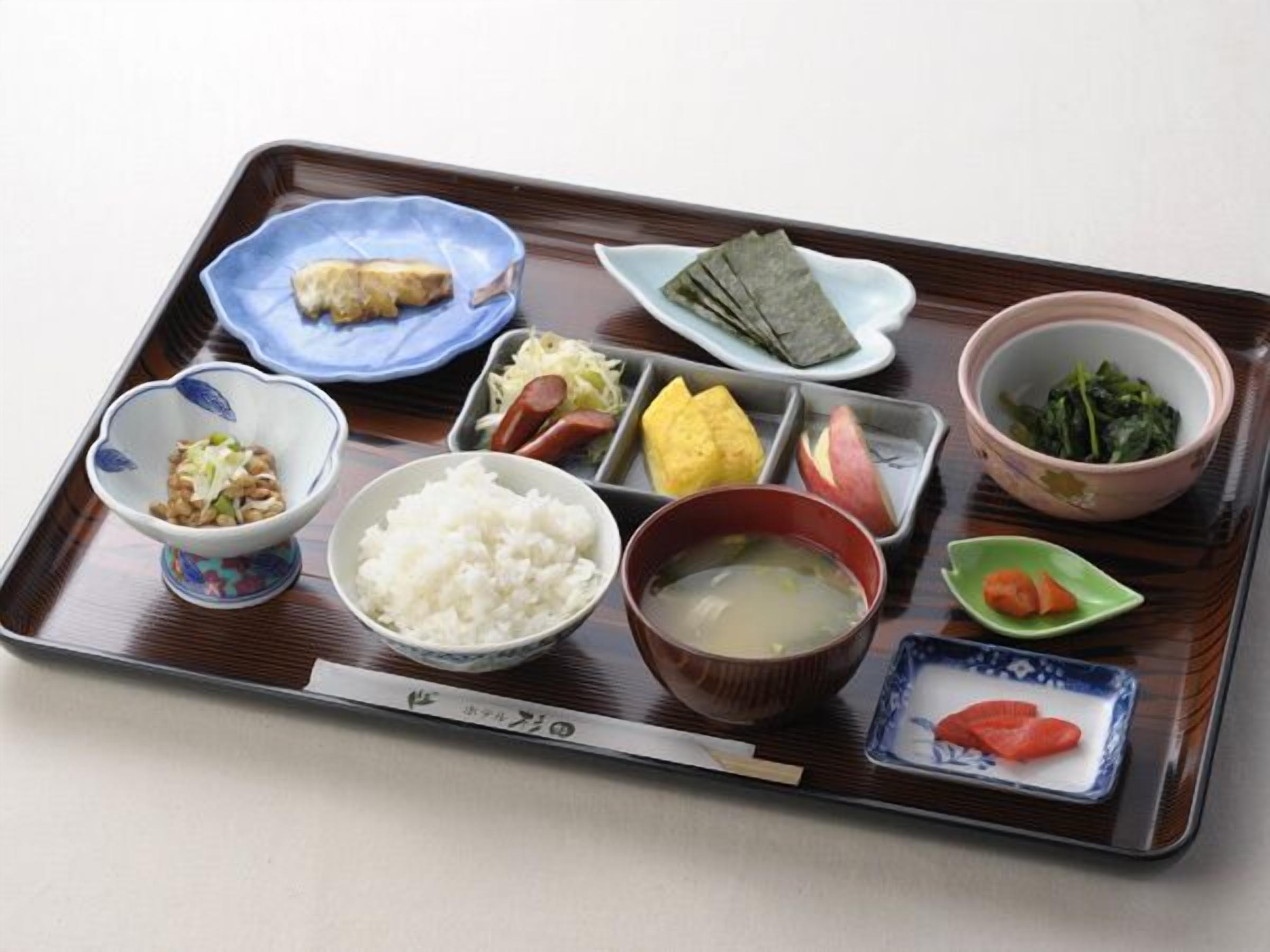 Comida tradicional japonesa presentada en una bandeja de madera con diversos platos, incluyendo arroz, sopa y vegetales encurtidos.