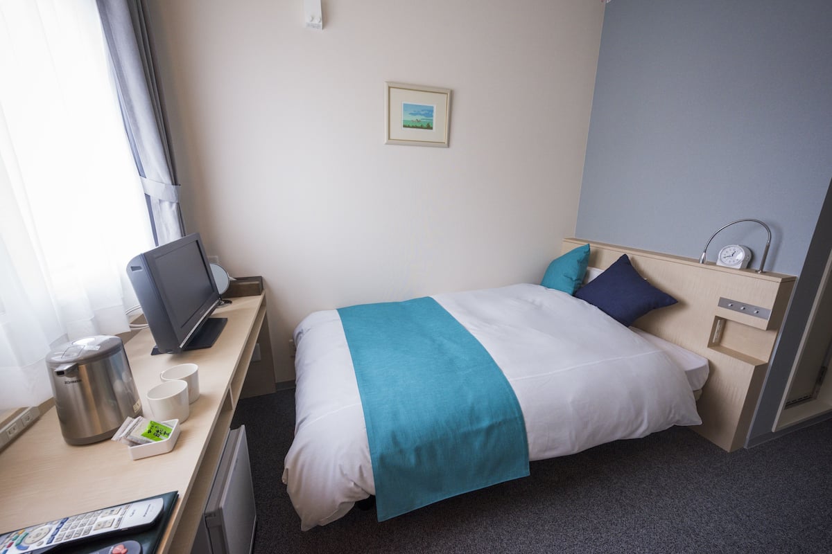 Une chambre d’hôtel équipée d’un lit, d’un bureau avec un ordinateur, d’une machine à café et d’une petite table avec des tasses et un menu.