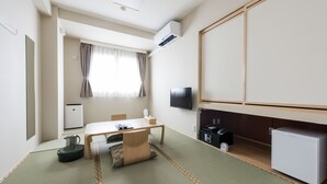 A compact hotel room with tatami flooring, a small table with a chair, a television, a mini-fridge, and a heater. - Hotel Sugita (Tomakomai)