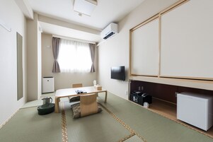 Habitación de hotel compacta con suelo de tatami, una mesa pequeña con una silla, televisor, minibar y calentador.