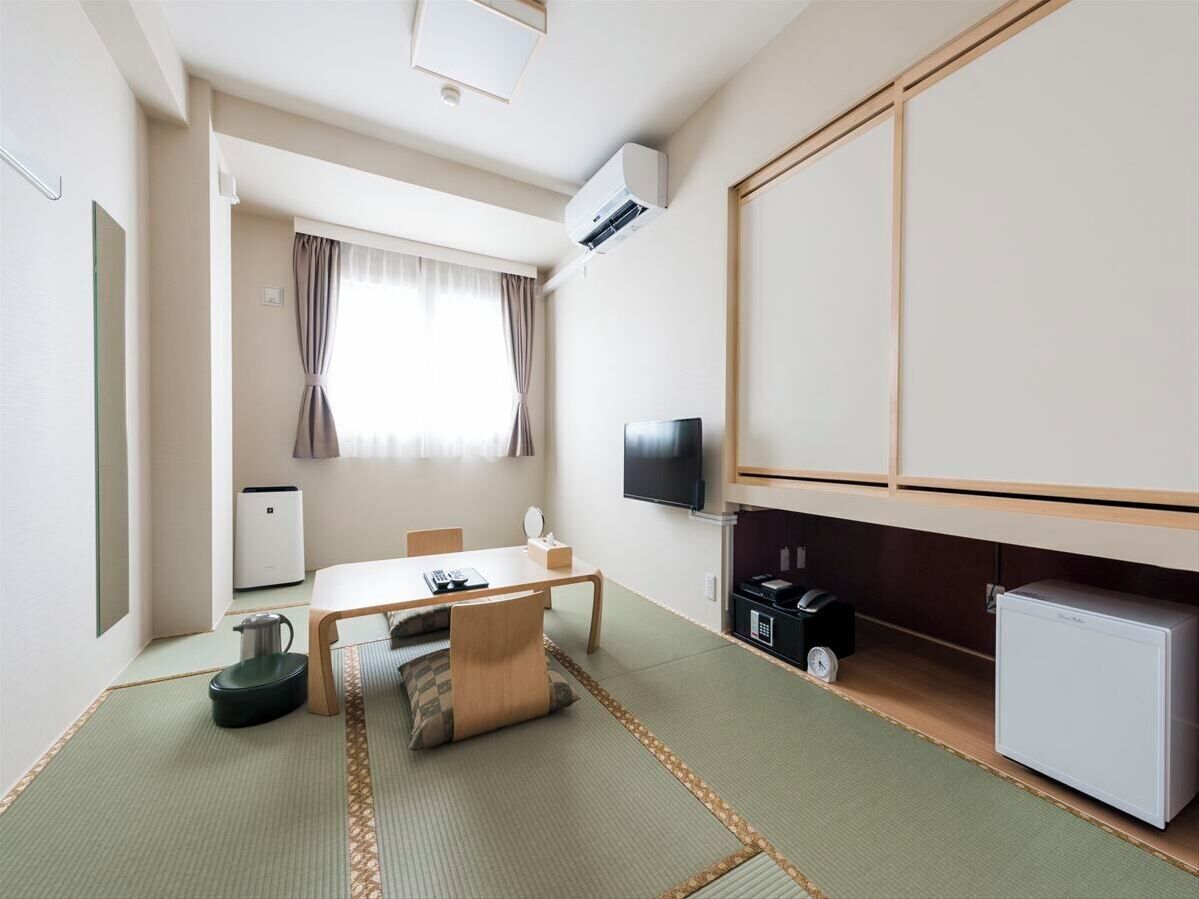 A hotel room with tatami flooring, a television, a small refrigerator, and a desk with a chair.