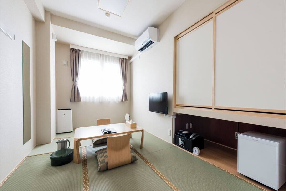Une chambre d’hôtel avec un sol recouvert de tatamis, une télévision, un petit réfrigérateur et un bureau avec une chaise.