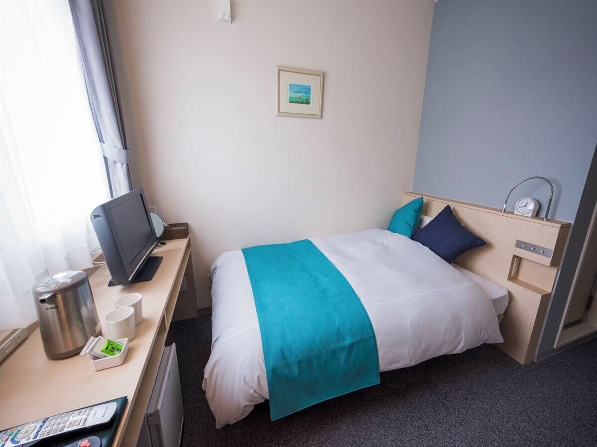 A hotel room with a bed, a desk with a coffee maker, a TV, and a small picture on the wall.