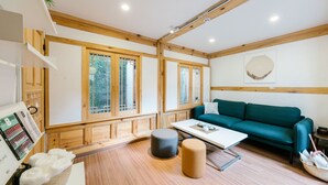 Ein Zimmer mit Holzbalken, einem grünen Sofa, einem weißen Tisch und einem Fenster mit Blick auf Grünflächen.
