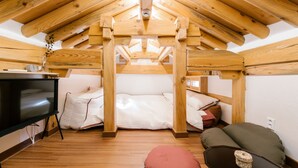 Ein gemütliches Schlafzimmer im Dachgeschoss mit Holzbalkendecke, einem Bett, einem Fernseher und einem kleinen Tisch.