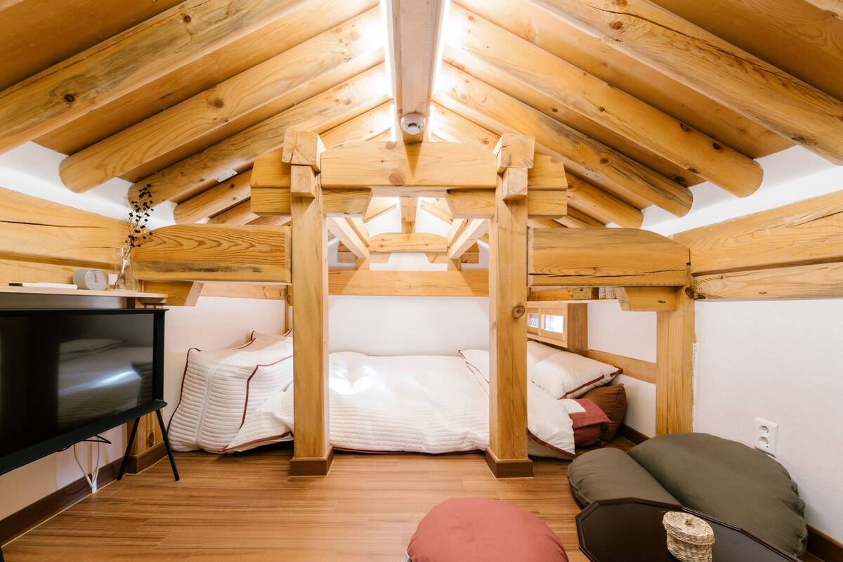 A cozy attic bedroom with a wooden ceiling, a bed, a TV, and a small table.