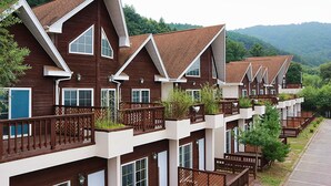 A row of multi-story wooden buildings with balconies, set against a backdrop of green hills. - Club Castle (Hoengseong)