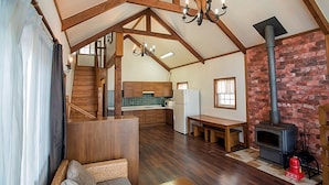 A spacious living area with wooden beams, a fireplace, a kitchen in the background, and a staircase leading to an upper level. - Club Castle (Hoengseong)