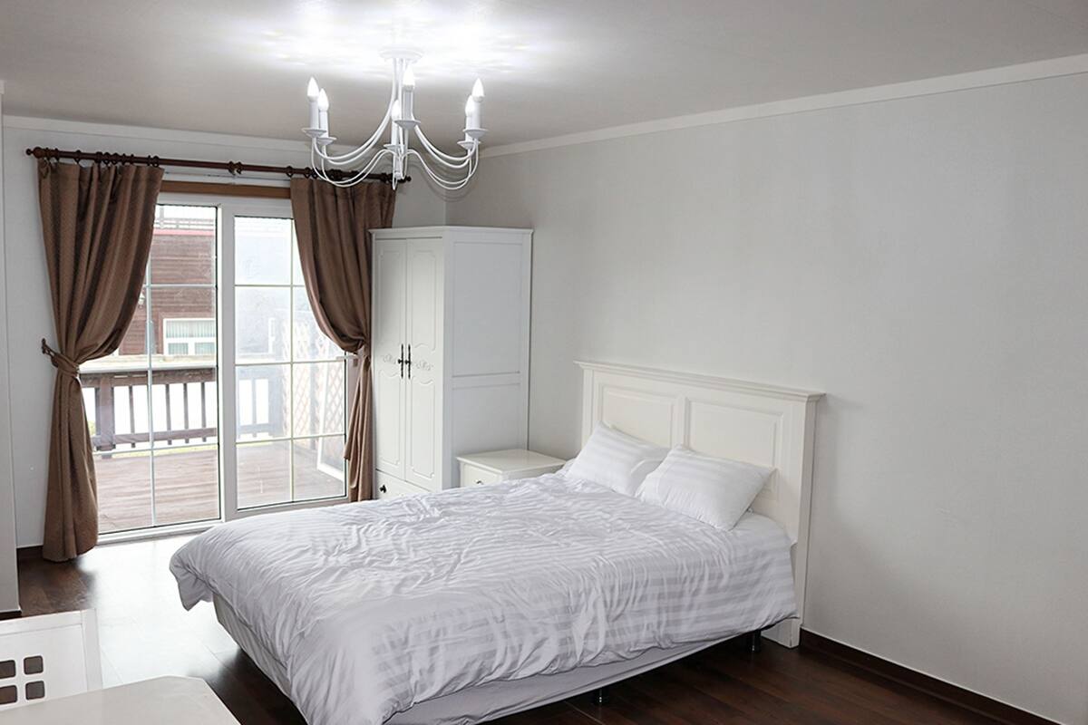 Ein Schlafzimmer mit Bett, Nachttisch, Kleiderschrank und einer Deckenleuchte.