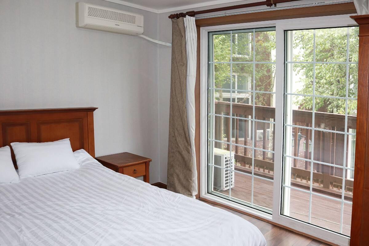 Ein Schlafzimmer mit großem Fenster, hölzernem Kopfteil und Nachttisch.