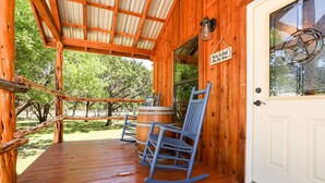 A wooden porch with rocking chairs, a wooden barrel, and a sign that reads "We're So Glad You're Here." - God's Country Cabins- Mercy I Close to Town (Fredericksburg)