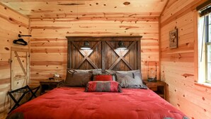 A cozy wooden cabin bedroom with a large bed, wooden walls, and a window. - God's Country Cabins- Mercy I Close to Town (Fredericksburg)
