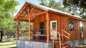 A rustic wooden cabin with a porch, a staircase, and a door. - God's Country Cabins- Mercy I Close to Town (Fredericksburg)