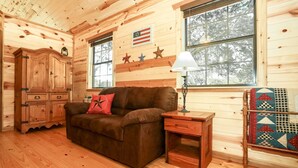 A cozy cabin interior with a brown sofa, wooden cabinet, and quilted wall hanging. - God's Country Cabins- Mercy I Close to Town (Fredericksburg)