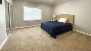Ein Schlafzimmer mit Bett, Nachttisch, Lampe, Fenster und Tür.