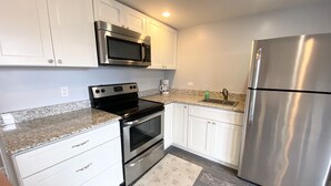 A kitchen with white cabinets, stainless steel appliances, a granite countertop, and a patterned rug. - 411 S. Madison Avenue (Watkins Glen)