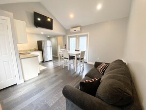 A modern kitchen with a built-in refrigerator, a dining area with a white table and chairs, and a gray sofa with patterned pillows. - 411 S. Madison Avenue (Watkins Glen)