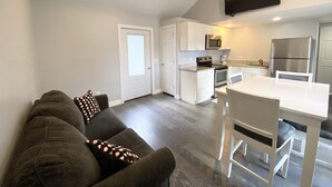 A modern kitchen with white cabinets, a stainless steel refrigerator, and a flat-screen TV mounted above the counter. - 411 S. Madison Avenue (Watkins Glen)