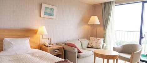 A hotel room with a bed, a sofa, a small table, and a balcony with a view.
