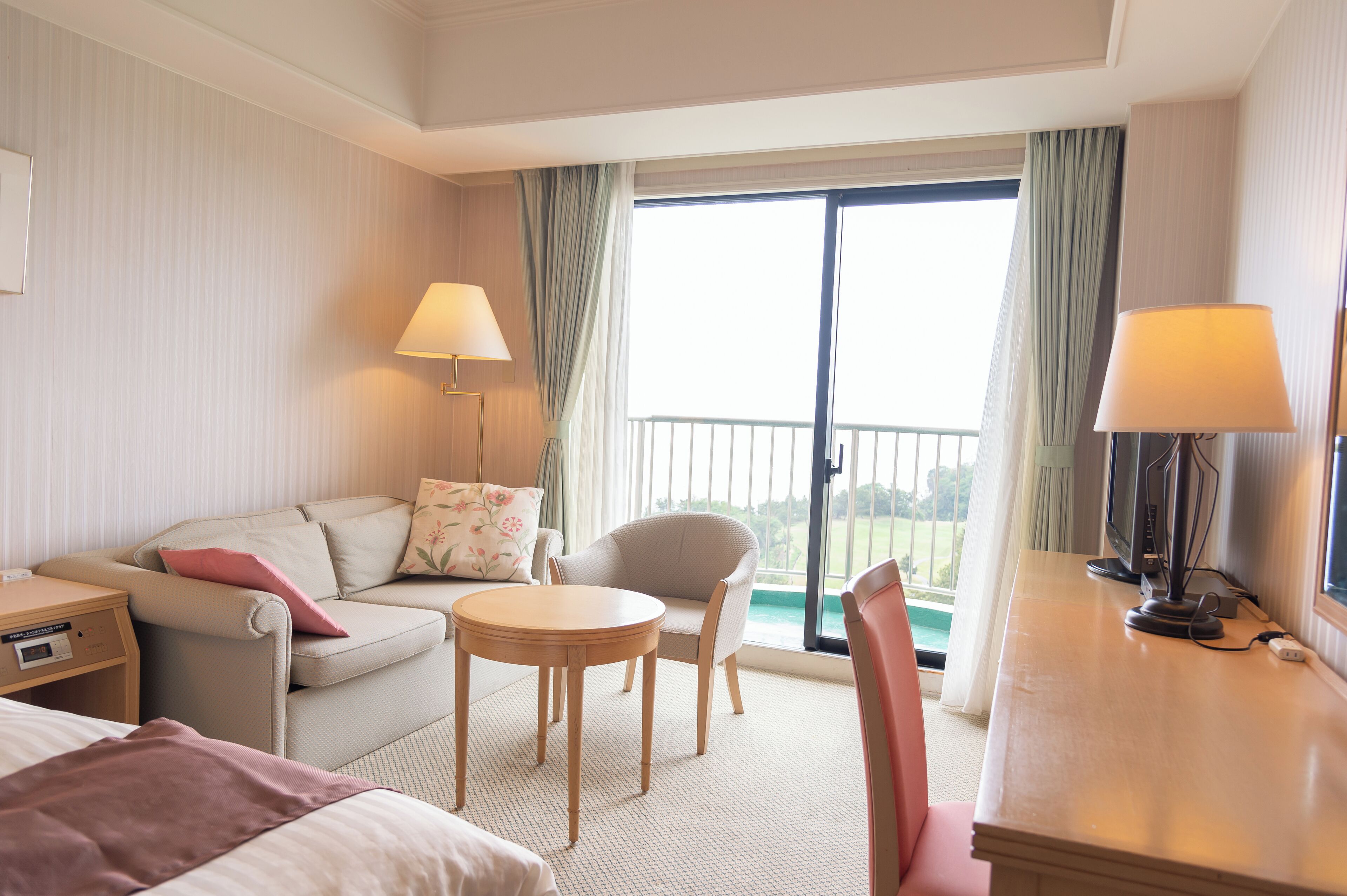 Een hotelkamer met een bank, fauteuil, klein tafeltje en een bureau met lamp.