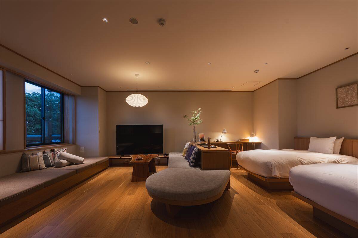 Una habitación de hotel moderna con un ventanal grande, un televisor de pantalla plana, un sofá, una cama y piso de madera.