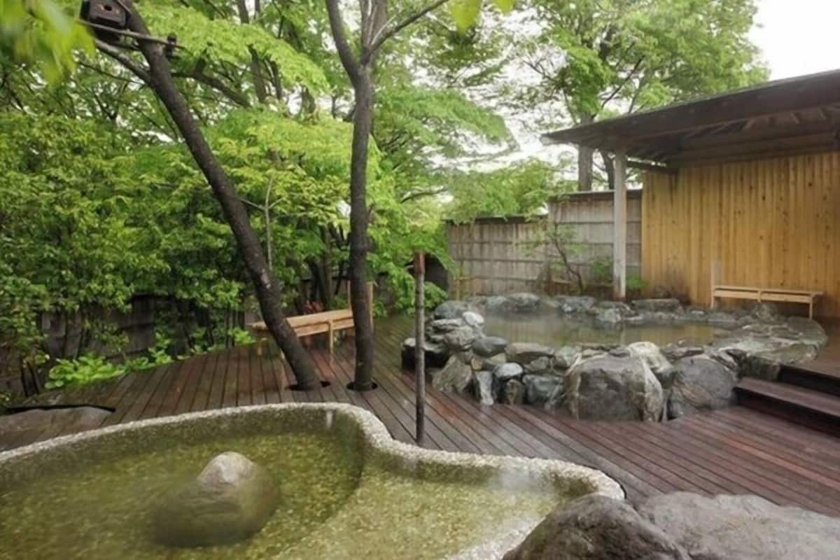 Un jardín japonés tradicional con terraza de madera, aguas termales y un edificio de madera.