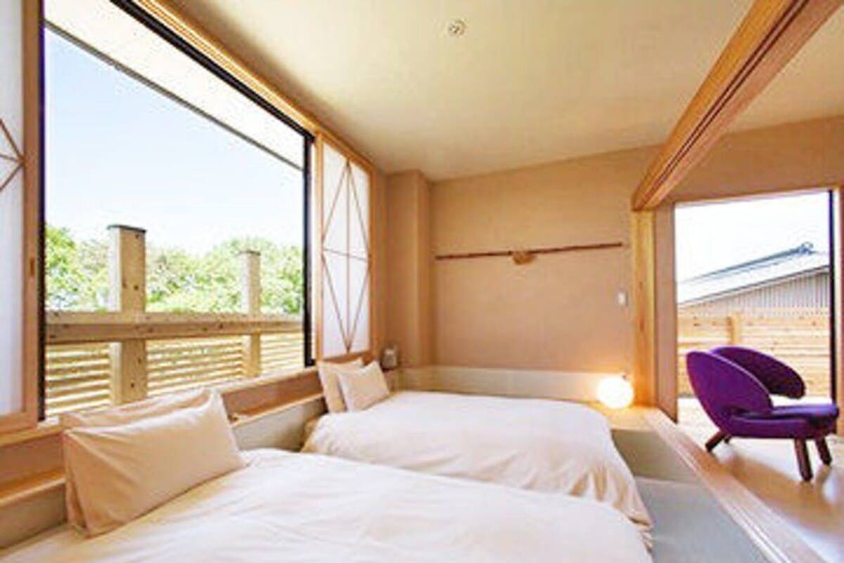 Una habitación con dos camas, una ventana, una silla y techo de madera.