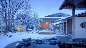 Un edificio tradicional japonés con jardín cubierto de nieve, estanque de carpas y una estructura de madera.