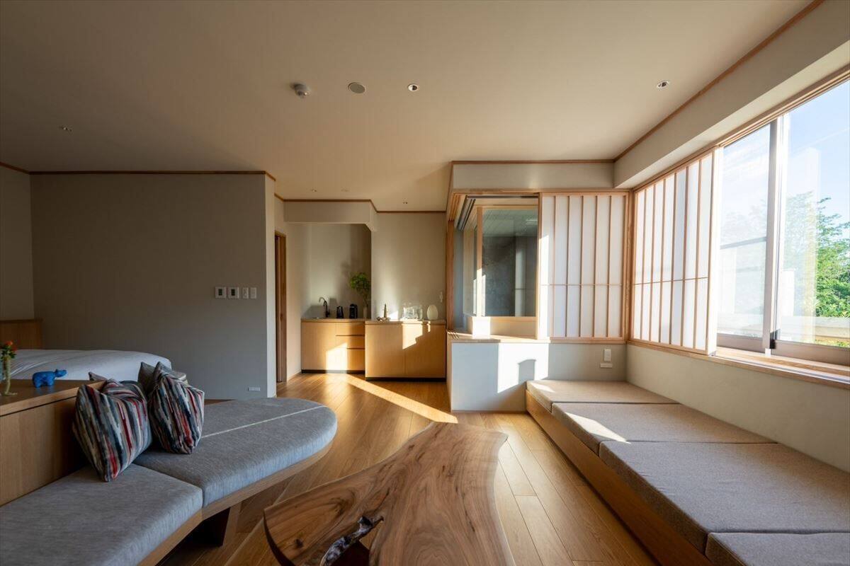 Un moderno salón con un sofá, una mesa de centro de madera y vistas a una cocina y zona de comedor a través de amplios ventanales.