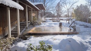 Un onsen japonés tradicional con estructura de madera, un baño de aguas termales y un paisaje nevado.