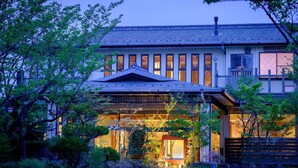 Un edificio tradicional japonés con una entrada amplia, un porche cubierto y un jardín con árboles y arbustos.