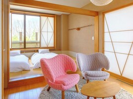 Una habitación con una cama, dos sillas, una mesa de madera y un ventanal con vistas a árboles.
