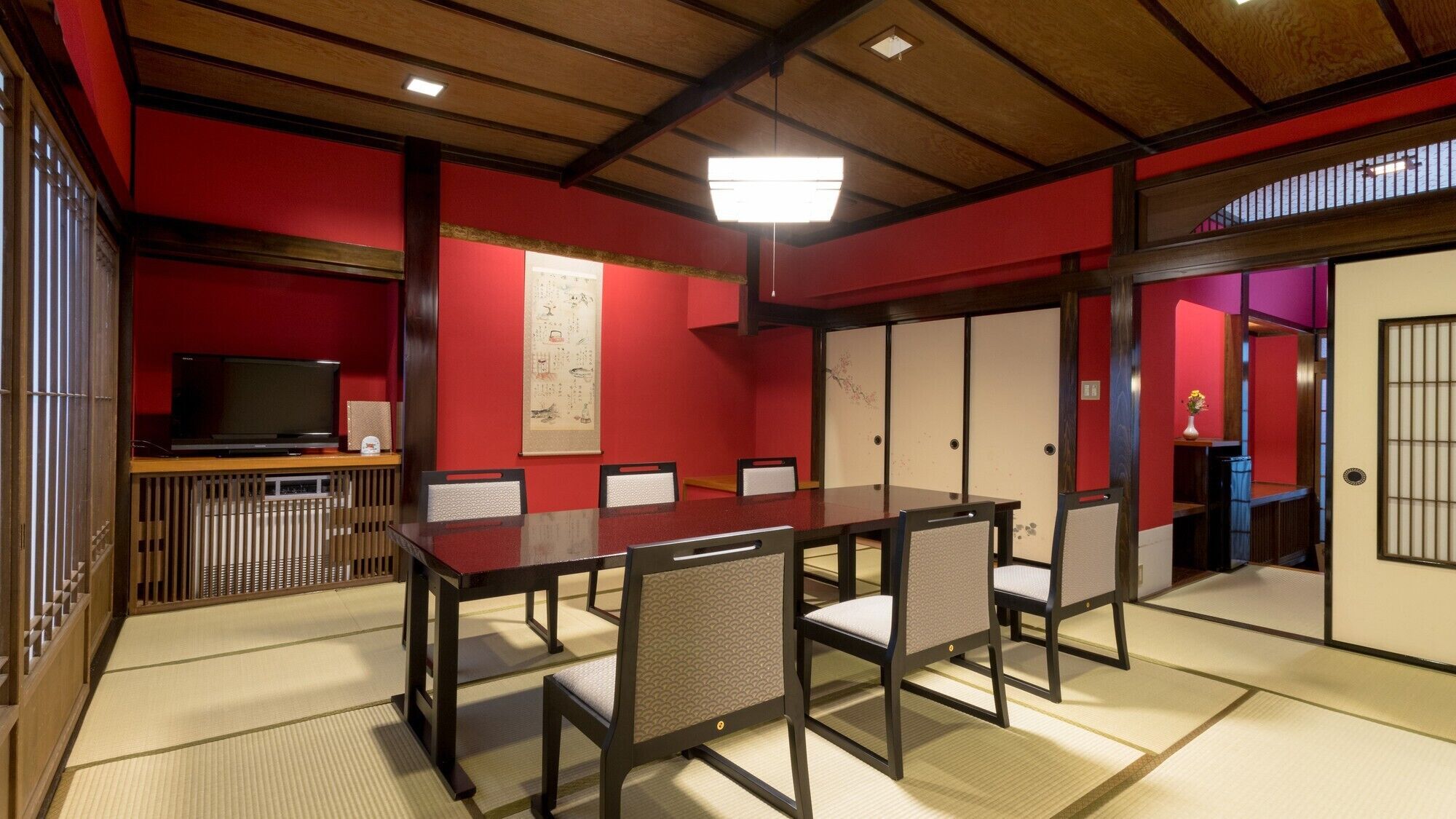 Una habitación tradicional japonesa con suelo de tatami, una mesa baja con sillas, un televisor y puertas correderas.