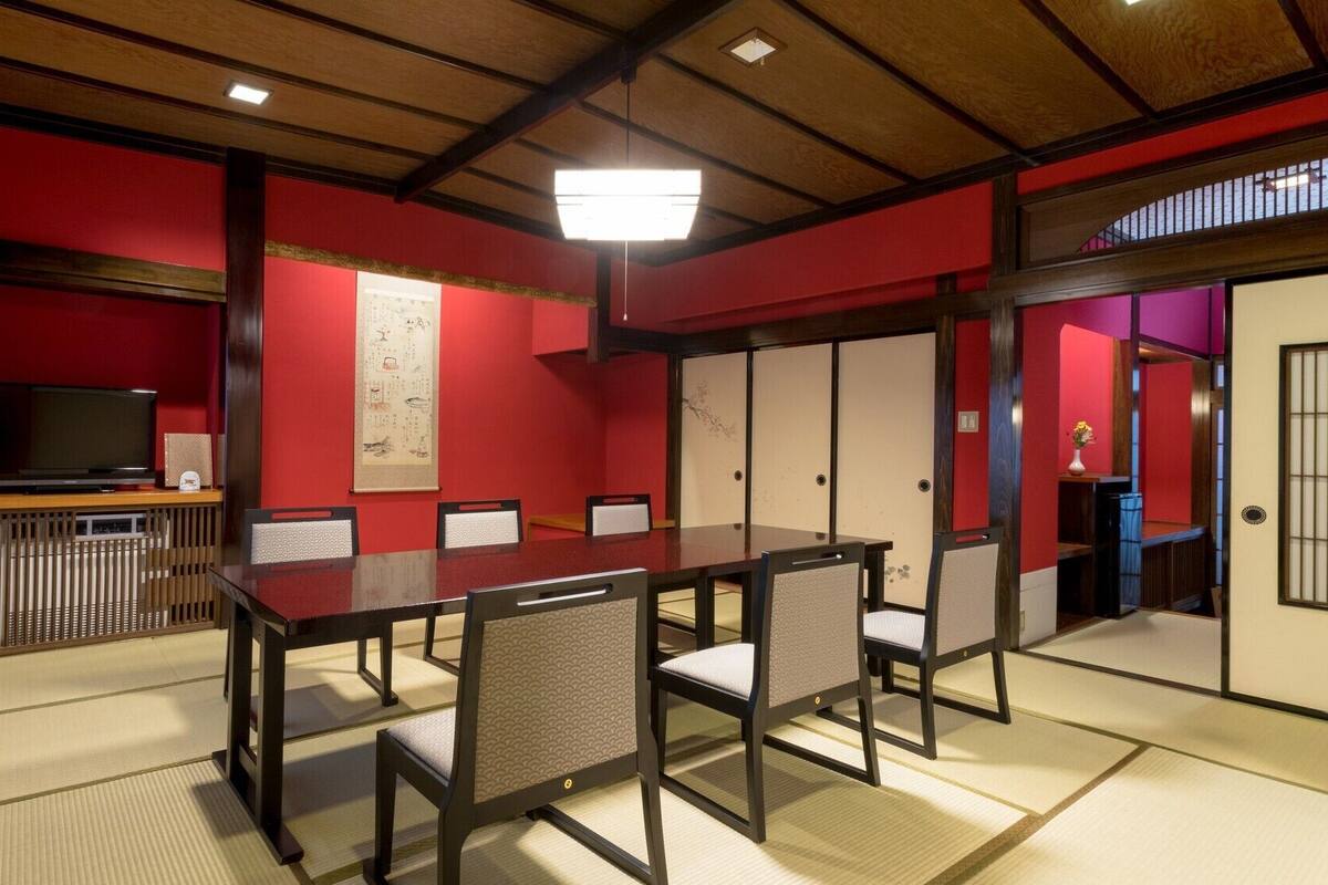 Una habitación tradicional japonesa con suelo de tatami, una mesa baja con sillas, un televisor y puertas correderas.