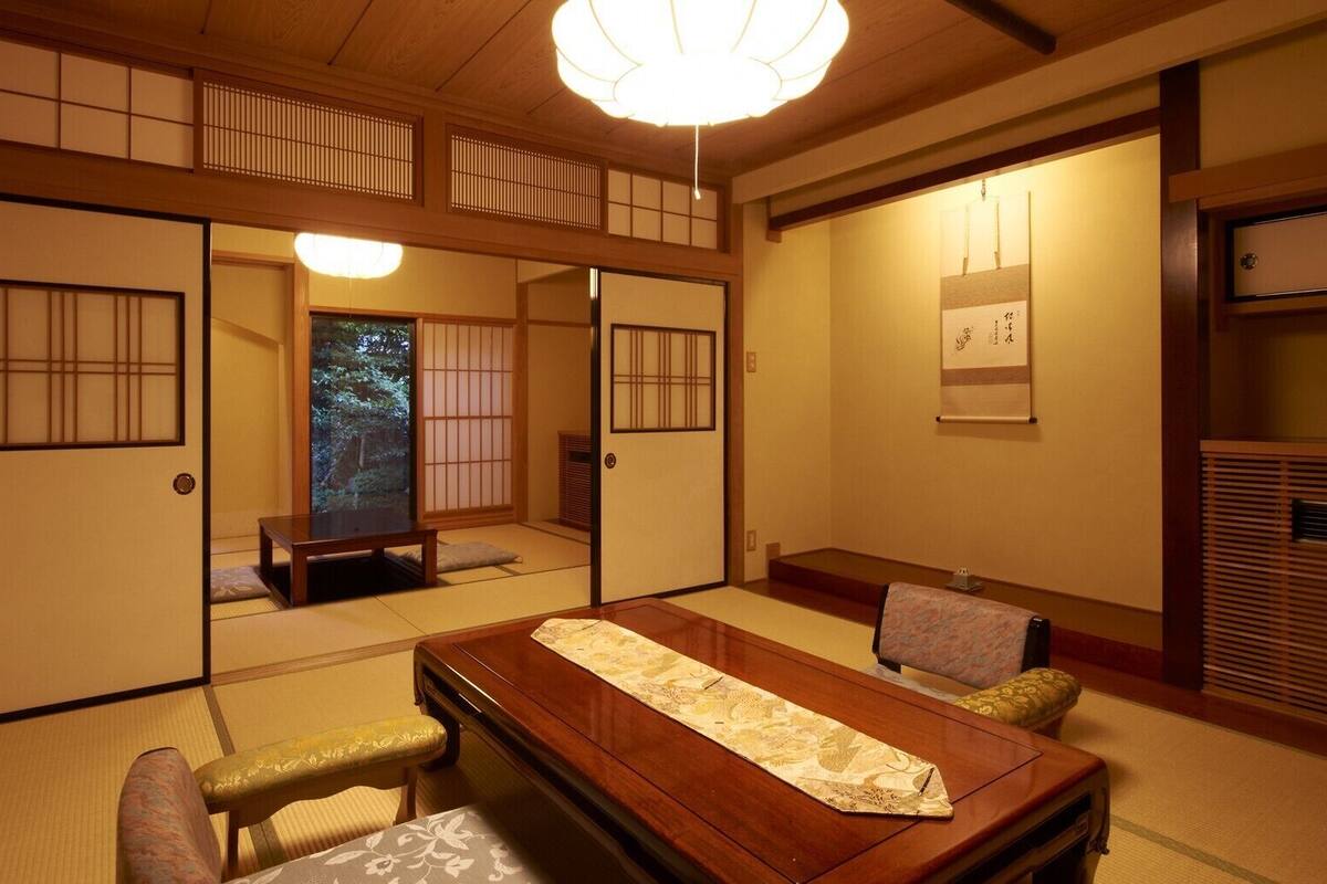 Una habitación japonesa tradicional con suelo de tatami, una mesa baja con un tapete decorativo, puertas correderas y una lámpara en el techo.