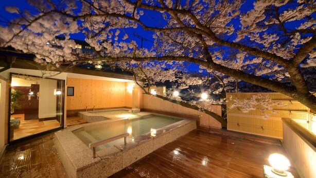A spa area with a hot tub, wooden walls, and cherry blossoms at night.