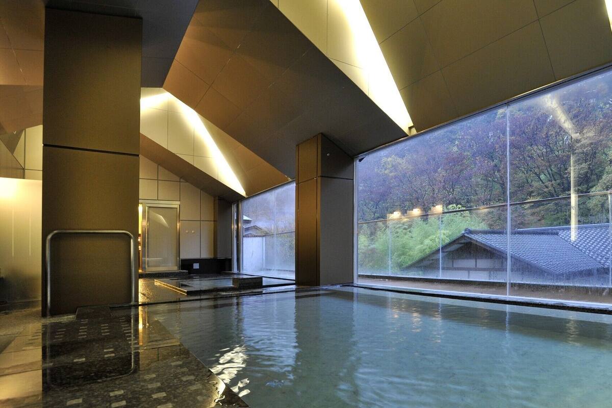 Una piscina interior moderna con un amplio ventanal que da a una construcción tradicional japonesa.