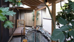 A traditional Japanese garden with a wooden structure, a stone water feature, and a wooden bench.