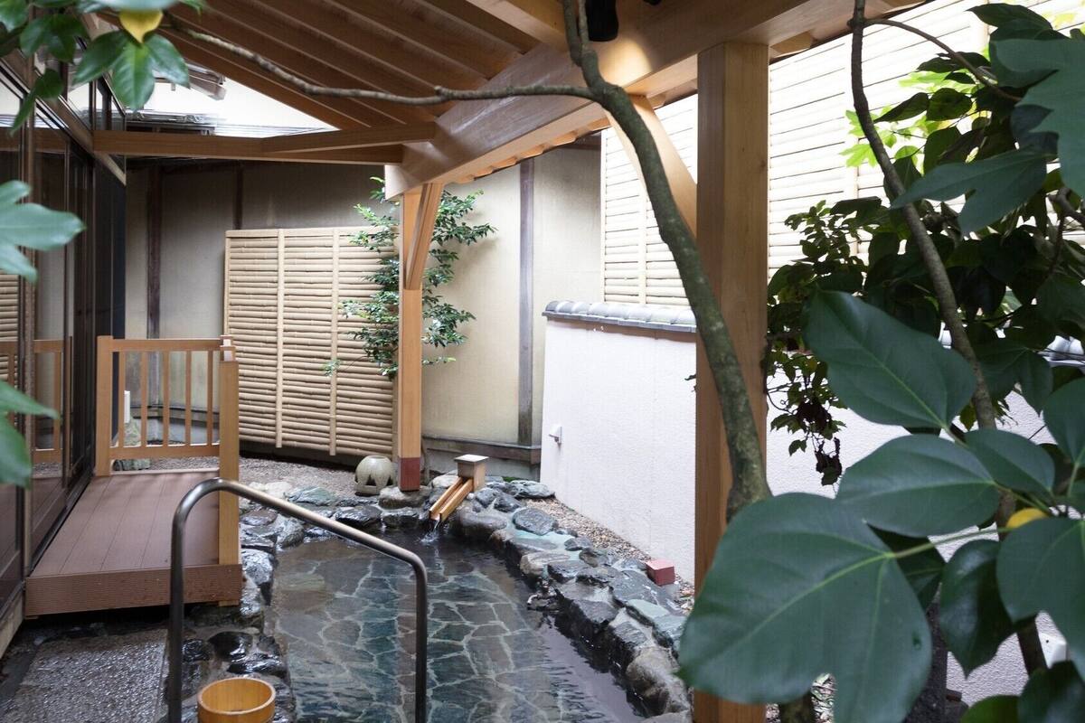 Un jardín japonés tradicional con una estructura de madera, un elemento decorativo de piedra con agua y un banco de madera.