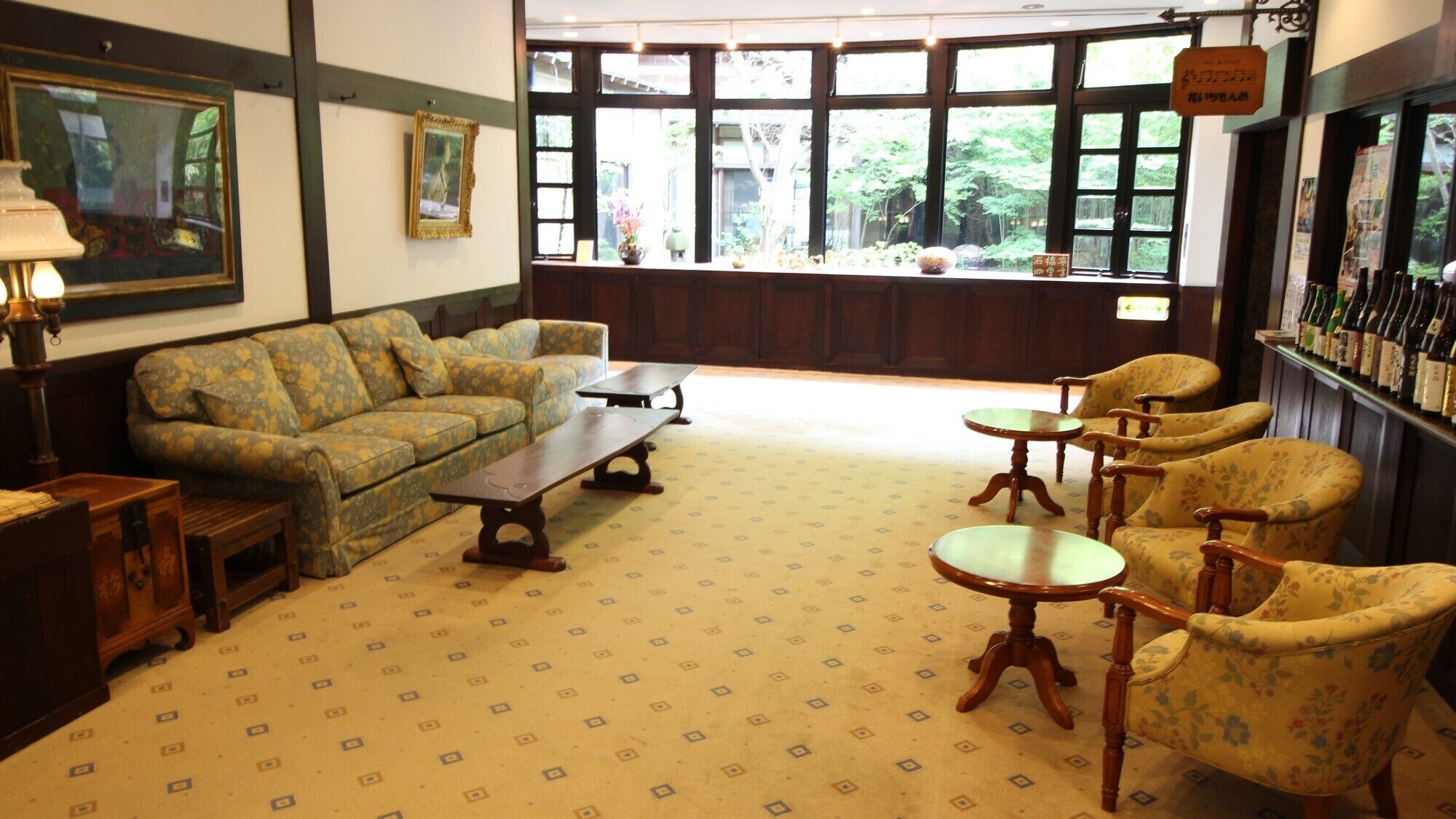 Una habitación con sofá, sillones, una mesa de centro, una lámpara y vistas a zonas verdes a través de amplios ventanales.