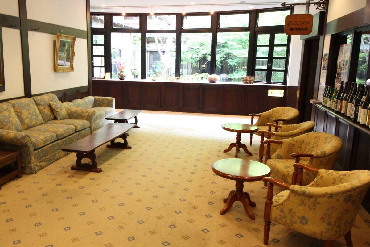 Una habitación con sofá, sillones, una mesa de centro, una lámpara y vistas a zonas verdes a través de amplios ventanales.
