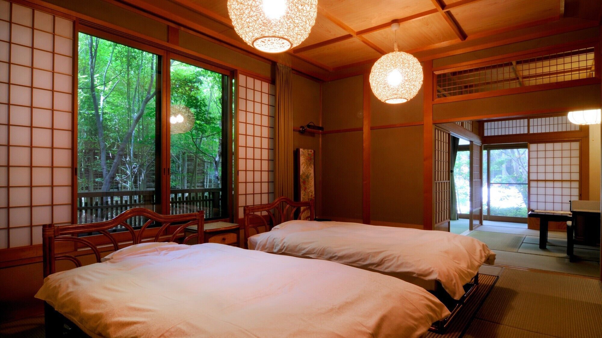 Una habitación japonesa tradicional con suelo de tatami, dos camas, puertas correderas y vistas a zonas verdes.