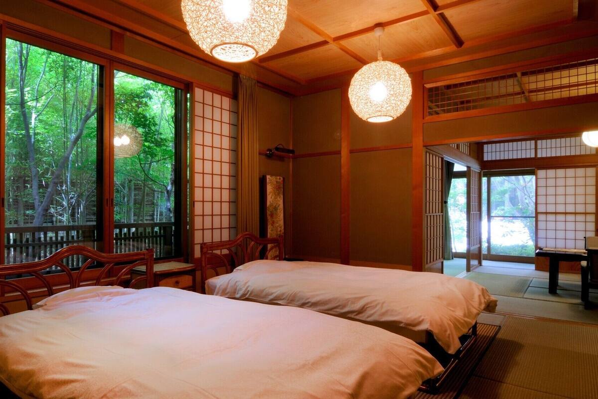 Una habitación japonesa tradicional con suelo de tatami, dos camas, puertas correderas y vistas a zonas verdes.