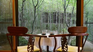 A table with a white tablecloth and two chairs with intricate back designs, set against a bamboo forest backdrop.