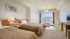 Une chambre d’hôtel avec deux lits, un bureau avec une télévision, une fenêtre donnant sur un beau paysage et un tableau accroché au mur.