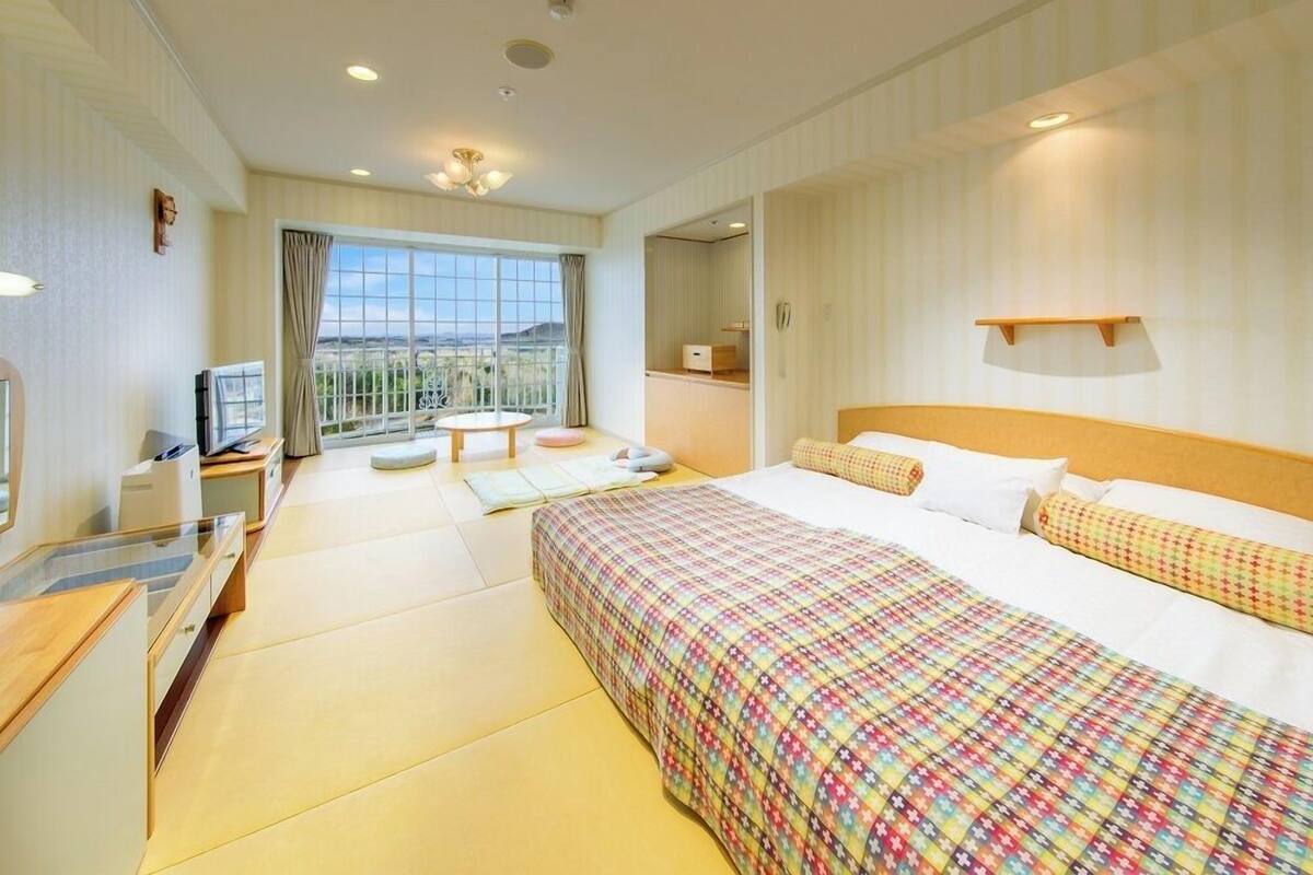 A hotel room with a bed, a desk, a chair, a small table, a TV, and a window with a view.
