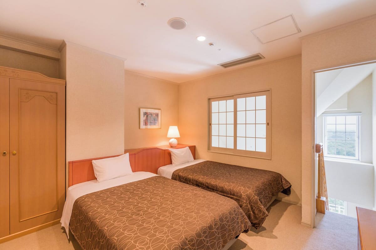 A hotel room with two beds, a window, a door, and a ceiling vent.