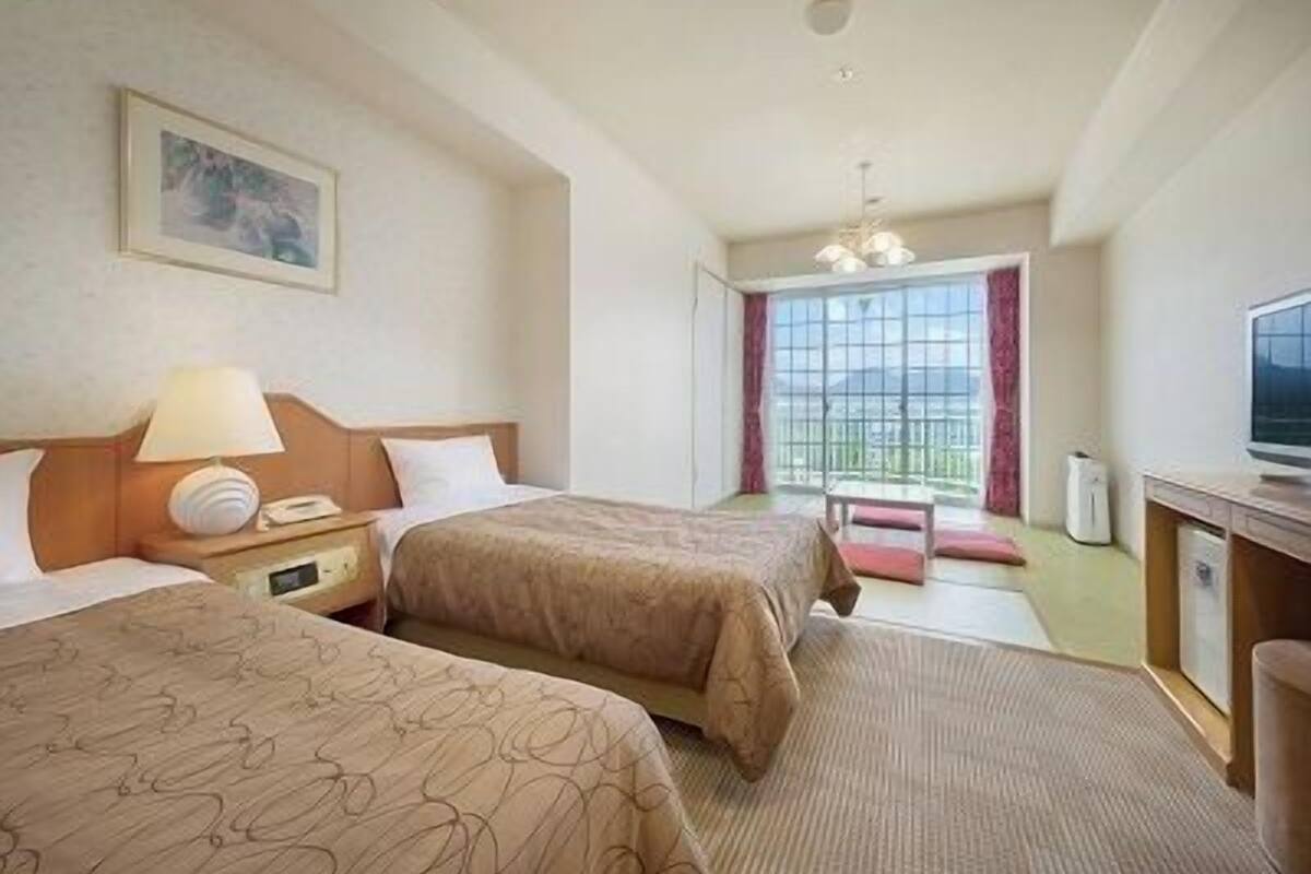A hotel room with two beds, a desk with a TV, a window with a view, and a painting on the wall.