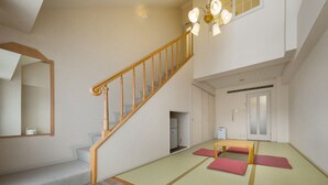 Une pièce spacieuse avec des tatamis, un escalier en bois et un luminaire de style japonais traditionnel au plafond.